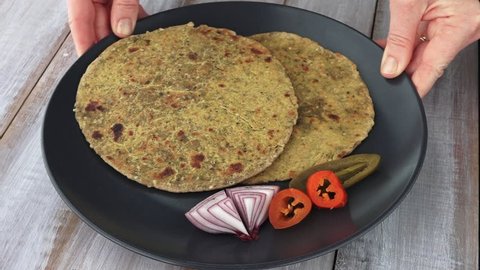Indian woman hands serving a Gujarati flatbread Methi Thepla. India food background and texture copy space