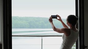 Silhouette of woman photographing lake from the window 