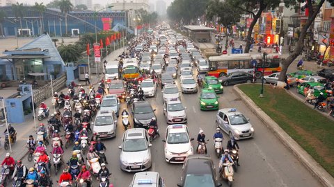 A crowded mess of motorbikes, cars and buses during rush hour at a big street in Hanoi, capitol of Vietnam. Wide shot.
