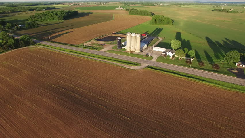 Rural Wisconsin landscape with silos, farms, fields, long shadows. Aerial view.

