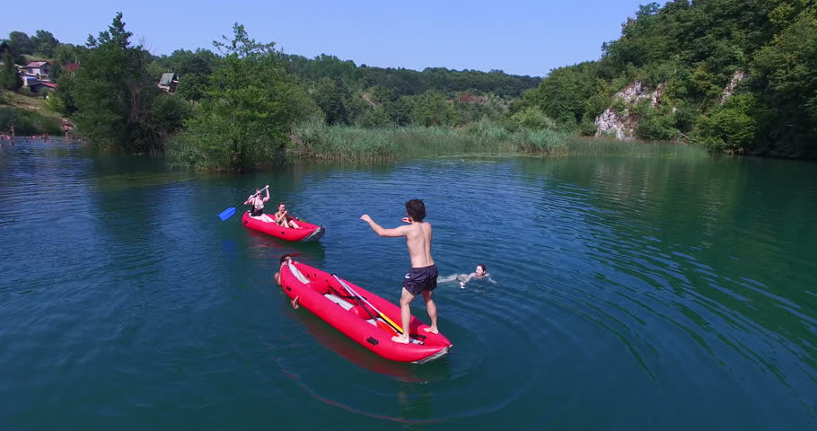 Aerial view of young man doing backflip from a canoe into river on beautiful summer day
