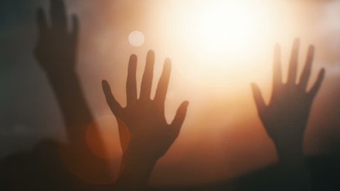 Silhouettes of hands raised in worship with light rays and Cross.