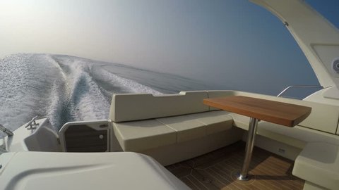 Stern of a boat navigating in the Mediterranean sea, with view of sofa and wooden table
