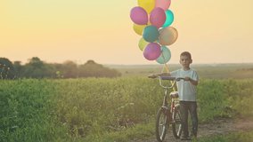 Little boy riding a bicycle in green field with balloons at sunset. RAW video record.