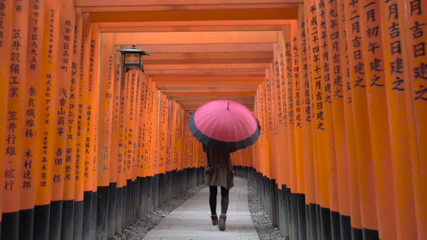 KYOTO, JAPAN - JANUARY 2016: Young woman walking through Torii Gates with umbrella, Fushimi Inari Shrine, Kyoto, Japan