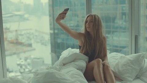 Young  teenage girl taking photo or making selfie  in her bedroom with french windows in the morning. Luxury apartment.