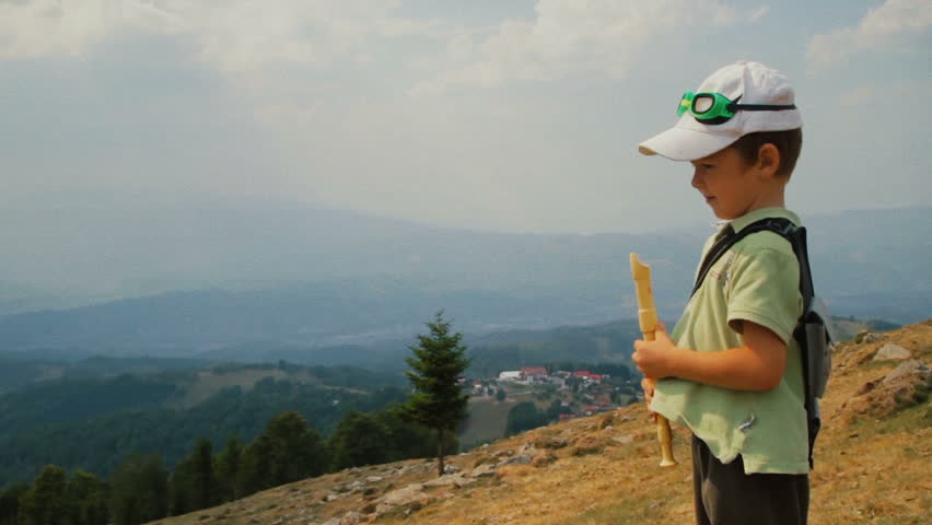 Little boy sitting on mountain peak and looking at green valley.