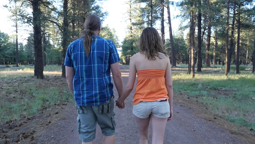 A tracking shot of a man & woman walking on a trail in the woods