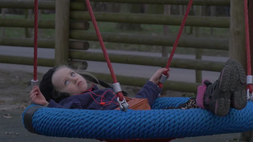 Girl Lies in a Nest Swing and Swaying Slowly. Kid is Playing on a Swing in a Park. Lies in the Nest. She