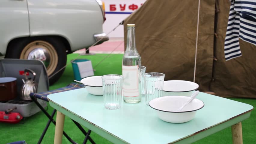 Small table with dishes, tent, burner and old car in pavilion at exhibition near inscription lunchroom.
