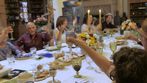 A man wearing a yarmulke leads a toast at a large dinner table such as a passover seder or jewish cultural event - handheld