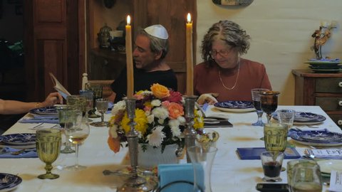 An older man reads from the haggadah at a passover seder and a woman has a small dog in her lap - dolly shot