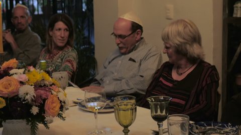 A man reads from a book (Haggadah) at a dinner table during a passover seder