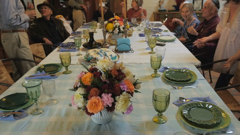 Pan up of a large table as guests arrive to a passover seder including men wearing yarmulkes.