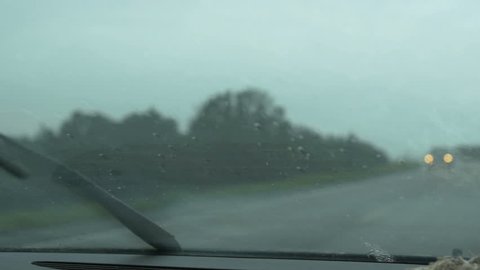 POV moving shot driving traveling down desert highway in storm rain with 3 cars passing by out of focus in slow motion