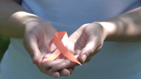Close-up shot of woman hands holding orange ribbon in sunlight. Leukemia, melanoma, multiple sclerosis, Self Injury Awareness Day