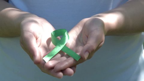 Close-up shot of woman hands holding green ribbon in sunlight. Kidney cancer, glaucoma, organ donation, depression, environmental protection awareness