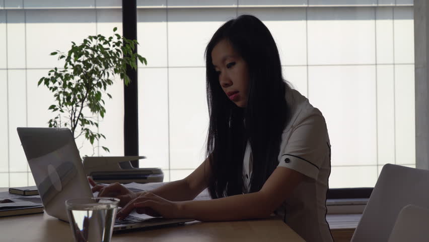 Attractive professional business woman typing on the computer. Successful manager in international holding or startup company reading documents. Female sitting at the big desk with glass of water