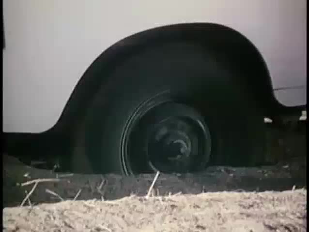 Close-up of car stuck on dirt road with back wheel spinning, 1970s