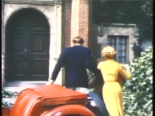 Rear view of couple hurrying into brick house, 1950s