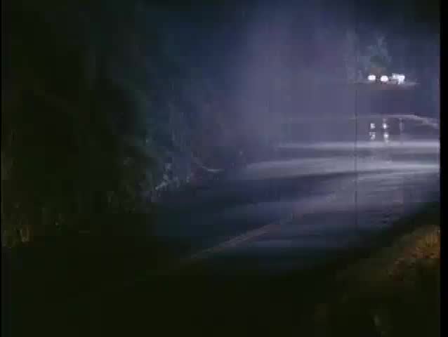 Car speeding down mountain road in the rain at night, 1970s