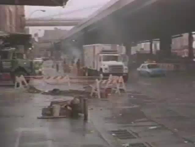 Ambulance following police car under New York City elevated train tracks, 1980s