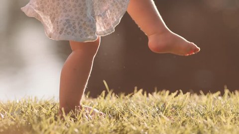 Little baby learns to walk. First Steps. Slow Motion 120 fps, 4K. Mother is teaching her child to do the first steps on a green grass in summer. Close up on feet. Happy childhood and Maternity. Family