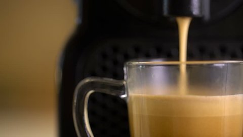 Macro shot of automatic coffee machine or coffeemaker pouring espresso coffee in a glass cup.