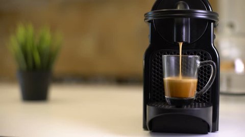Automatic coffee machine or coffeemaker pouring espresso coffee at home in a glass cup.