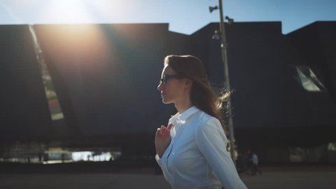 Side view of young successful businesswoman wearing modern suit and walking in the city at break, flare light, sunshine,  slow motion