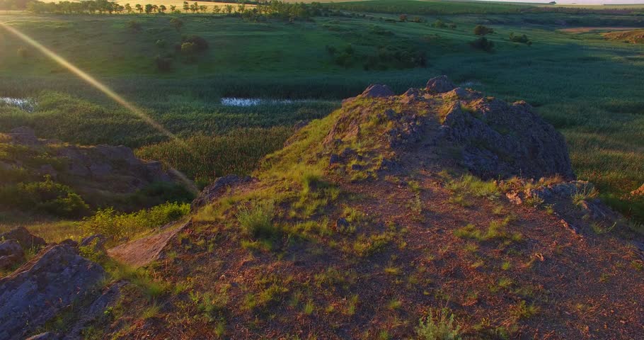 Aerial view. Dawn on the prairie. Flying over the swampy river with rocky shores flowing through the prairie, at sunrise.