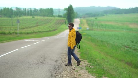man hitchhiking in the countryside, he walk on an empty road without cars