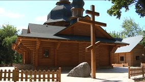 a Temple of All Sacred is Recorded on Video. the Temple is Built Entirely of Wood Beams. the Large Wooden Cross Stands in Front of the Temple. a Temple is Protected by a Low Wooden Fence.
