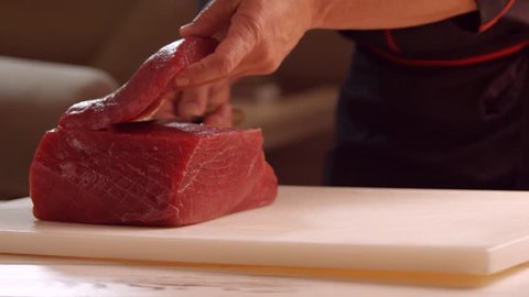 Hands with knife cut meat. Knife cutting meat on board. Chef starts cooking salmon. Even pieces of raw fish.