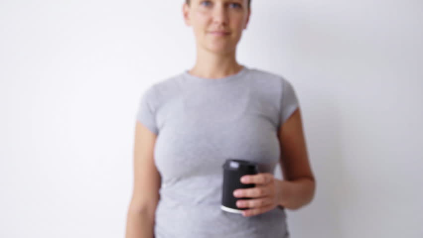 Unfocused handsome girl in blank shirt shows black paper cup on camera smiling