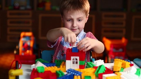 Boy Builds a House Out of Colored Blocks of Lego at the Table
