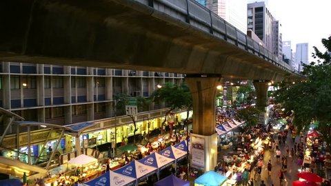 BANGKOK, THAILAND CIRCA JULY 2016, Sathon Sunday night street market from overhead with passing sky-train above with food stalls, crowds of people, lights and edge of bridge. 