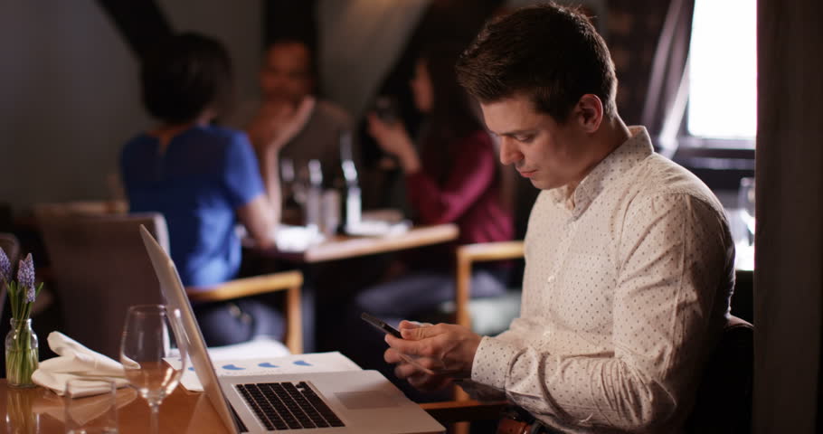 4K Young professional man working on laptop & talking on phone in relaxed bar setting | Shutterstock HD Video #17549083