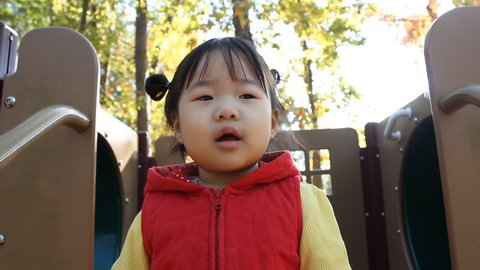 Beautiful Baby Asian Toddler Girl in Red Vest Babbling atop playset