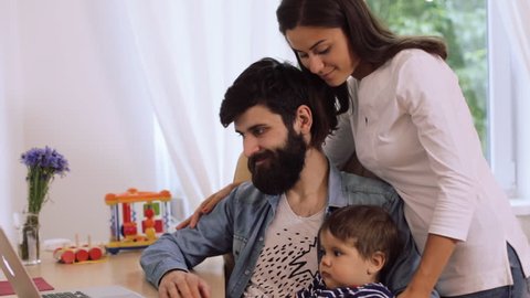 Happy young couple with son using laptop at desk, young woman kissing bearded man