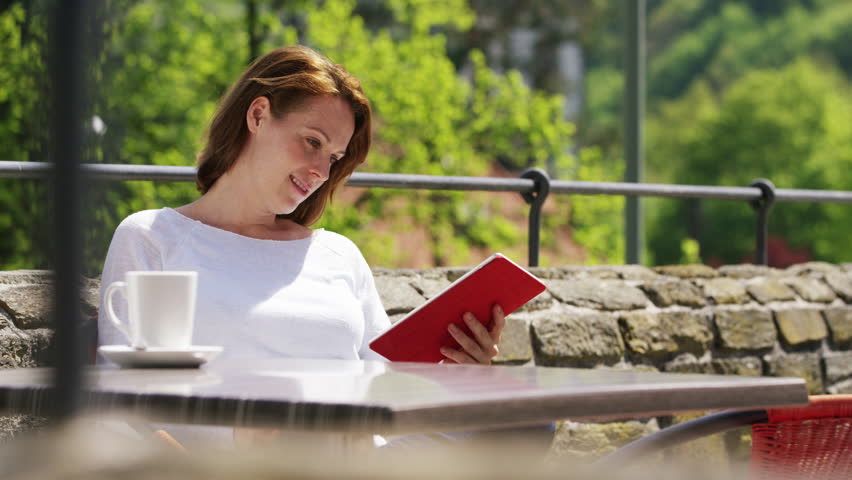 Casual woman sitting in a beautiful beer garden surfing on her tablet