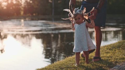 Little baby learns to walk. First Steps. Slow Motion 120 fps, 4K. Father is teaching his child to do the first steps on a green grass in summer. Close up on feet. Happy childhood and Parenthood.