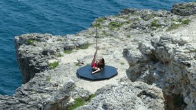 Pole dancing as an alternative fitness young woman dancer in black red bodysuit performs tricks and spins on rocky cliff above the sea extreme long shot episode_7
