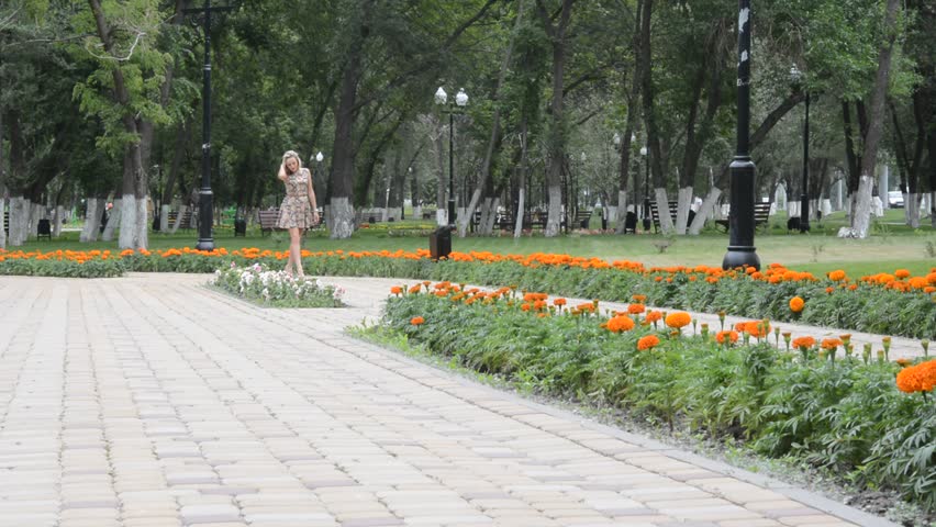 A young blonde girl in dress posing in summer Park
