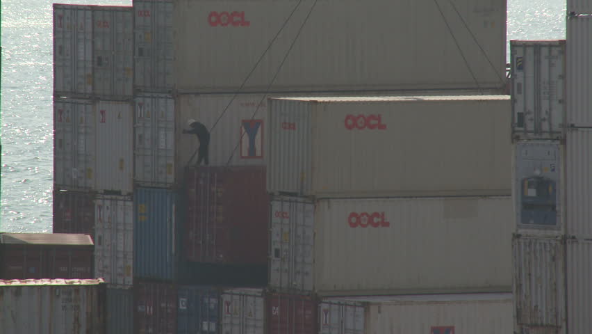 HONG KONG - CIRCA JUNE 2010: Dock worker guides shipping containers into place