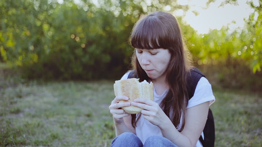 Young girl spending a day in nature and eating a sandwich at sunset
