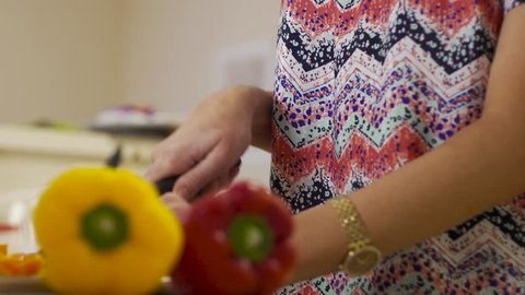 Camera jibs up then down as the young woman cuts peppers in the kitchen for the family dinner 
