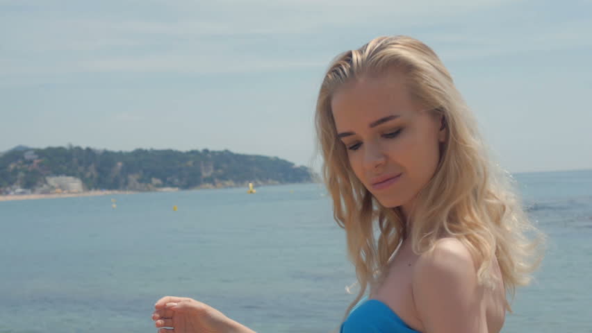 Portrait of attractive woman standing at beach. Happy smiling girl looking at camera at seaside. Young blonde woman relaxing at beach.
