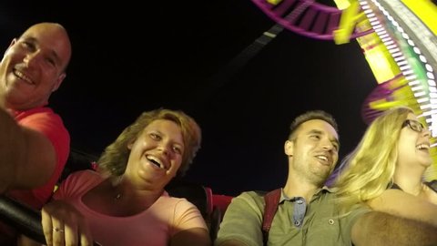 Group of excited people having fun on roller coaster ride in amusement park at night.
