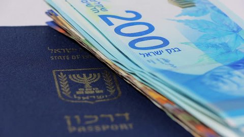 Stack of israeli money bills of 200 shekel and israeli passport - Pan left
